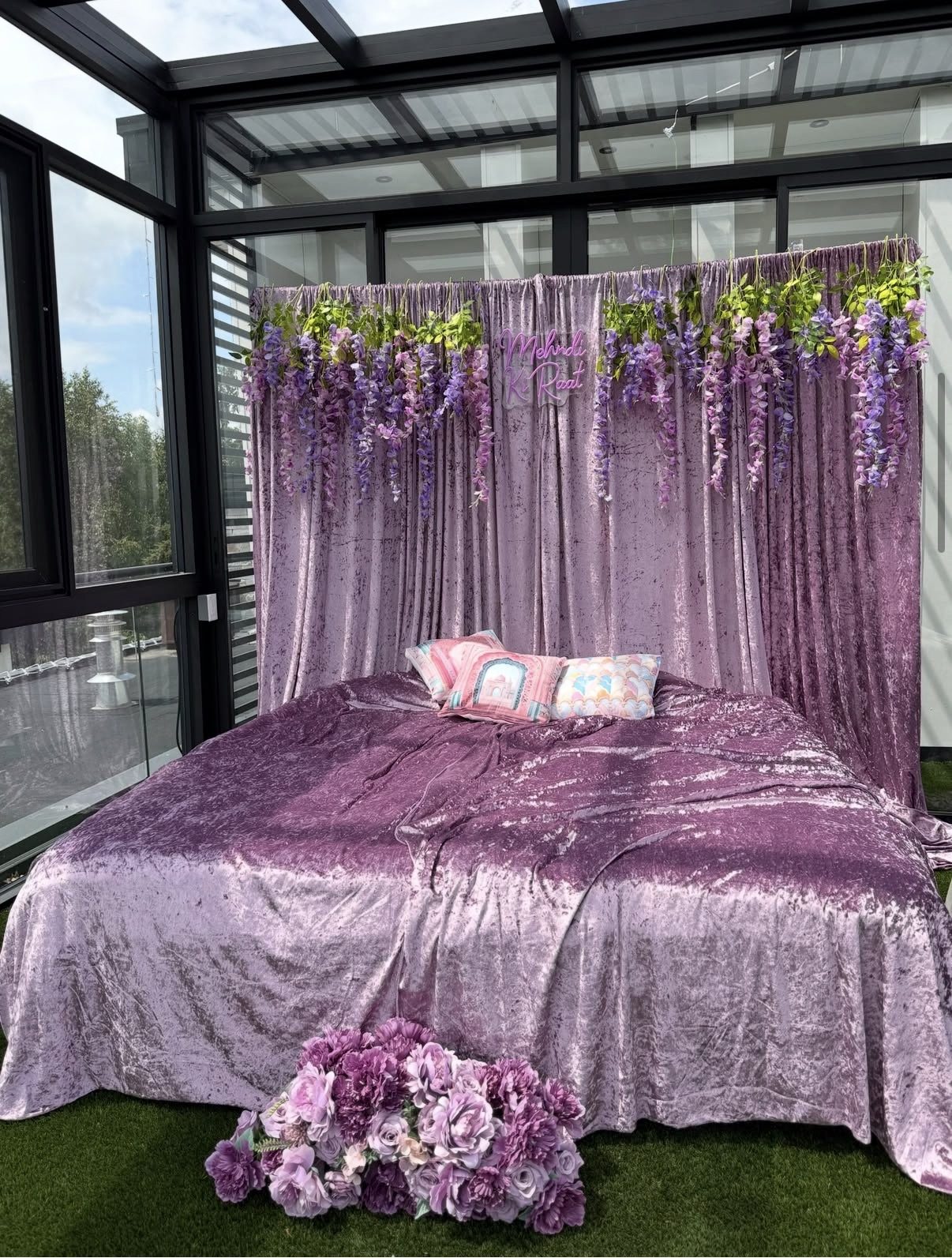 Mehndi night decor in Surrey — lavender crushed velvet backdrop, wisteria florals and neon sign by The Setup Studio