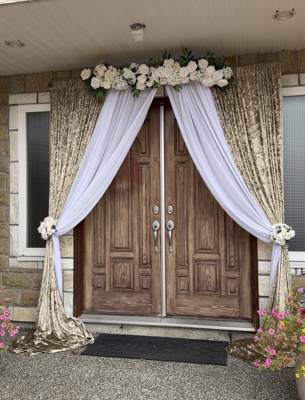 A front entrance draped in gold crushed velvet and white chiffon with a white floral swag