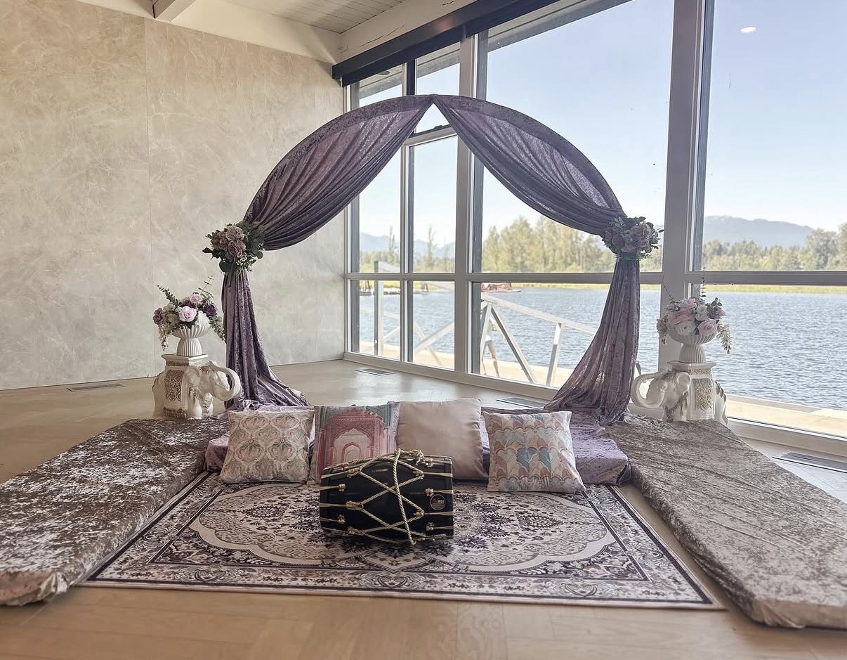 Mehndi lounge with a mauve crushed-velvet draped arch, floor seating, Persian rug and a dholki