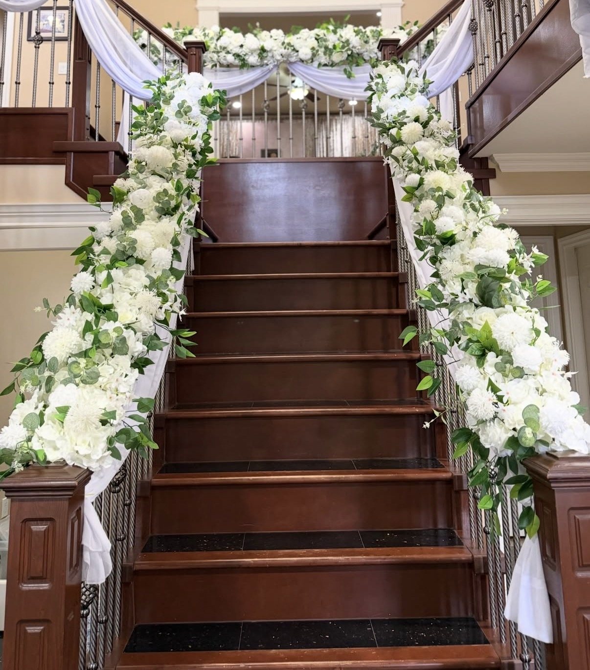 A staircase banister dressed with white florals, greenery garland and white drapery