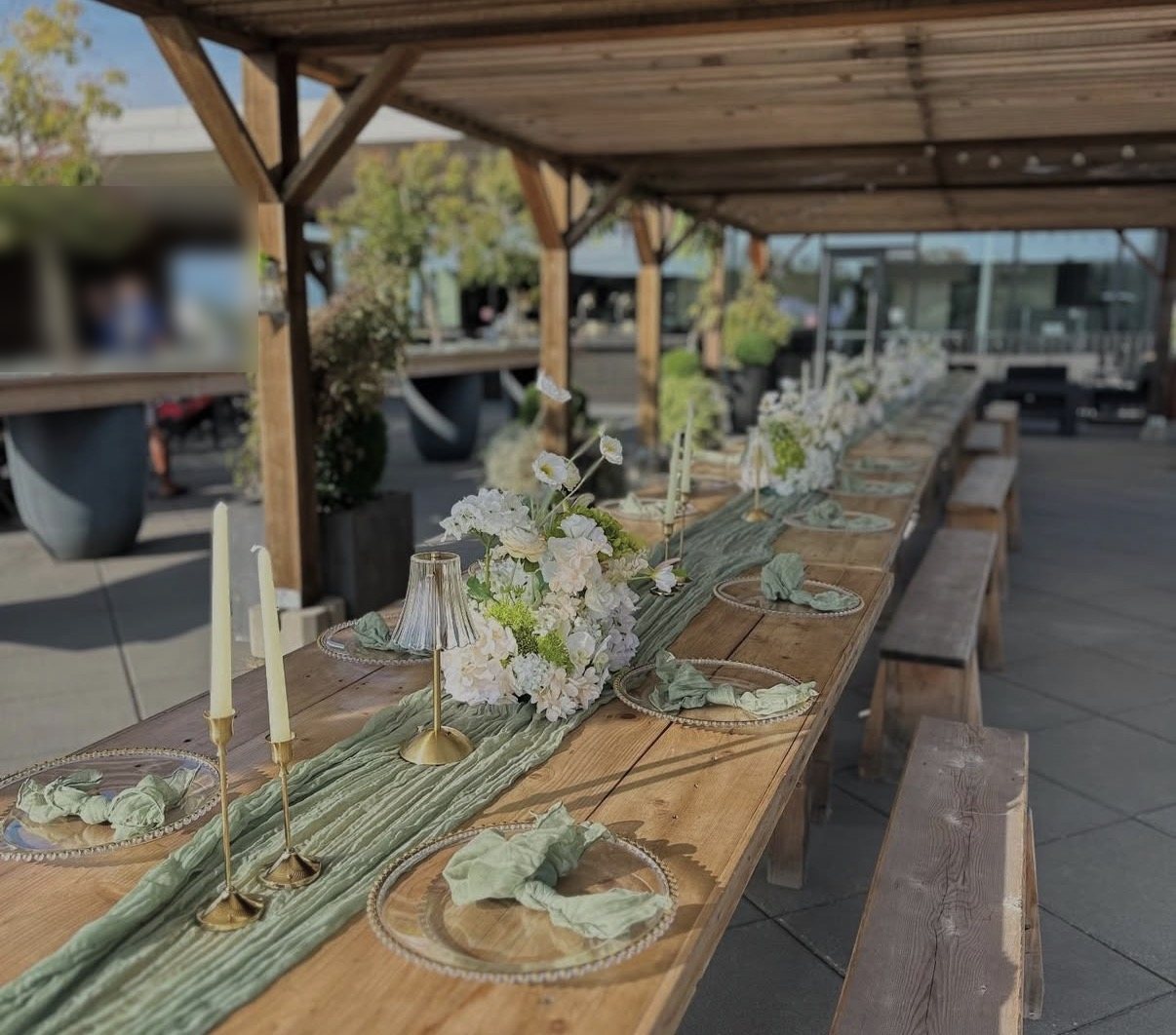 A long farm table with sage cheesecloth runner, gold candlesticks, beaded chargers and sage napkins