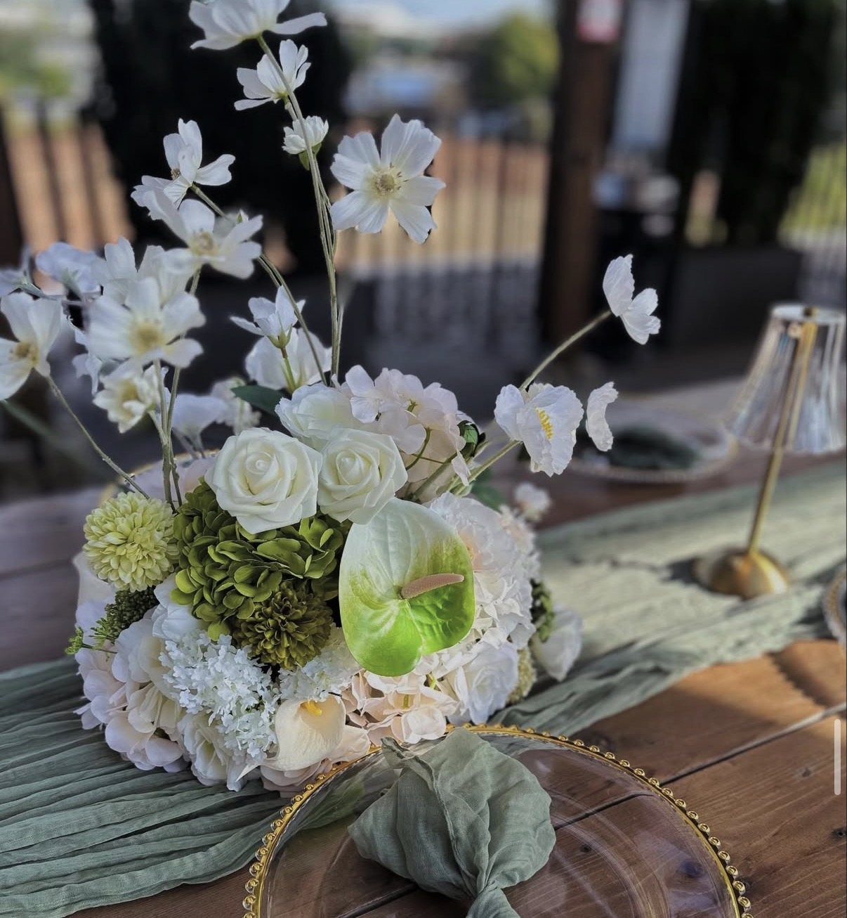 White and green silk floral centrepiece on a sage runner with a gold beaded charger