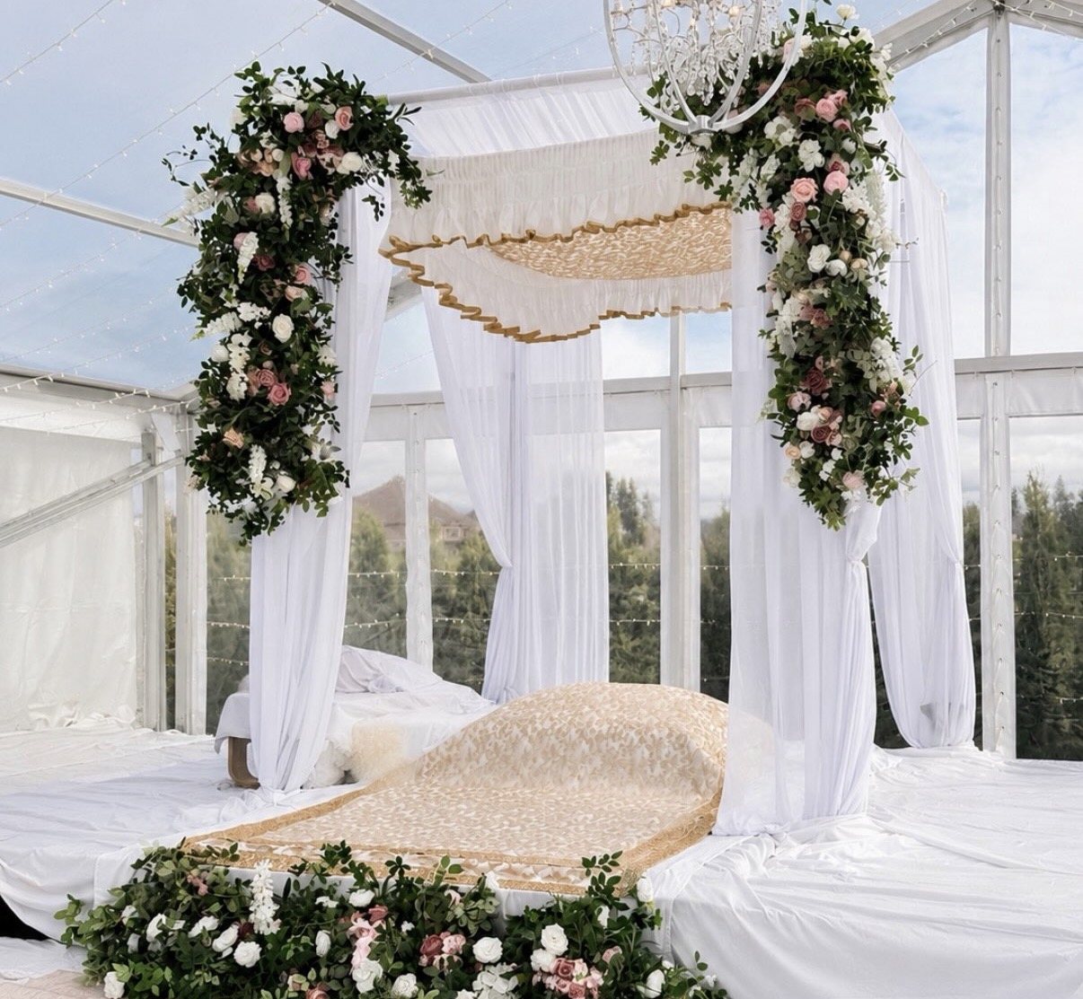 White canopy with greenery and blush florals over a gold-overlaid ceremony bed