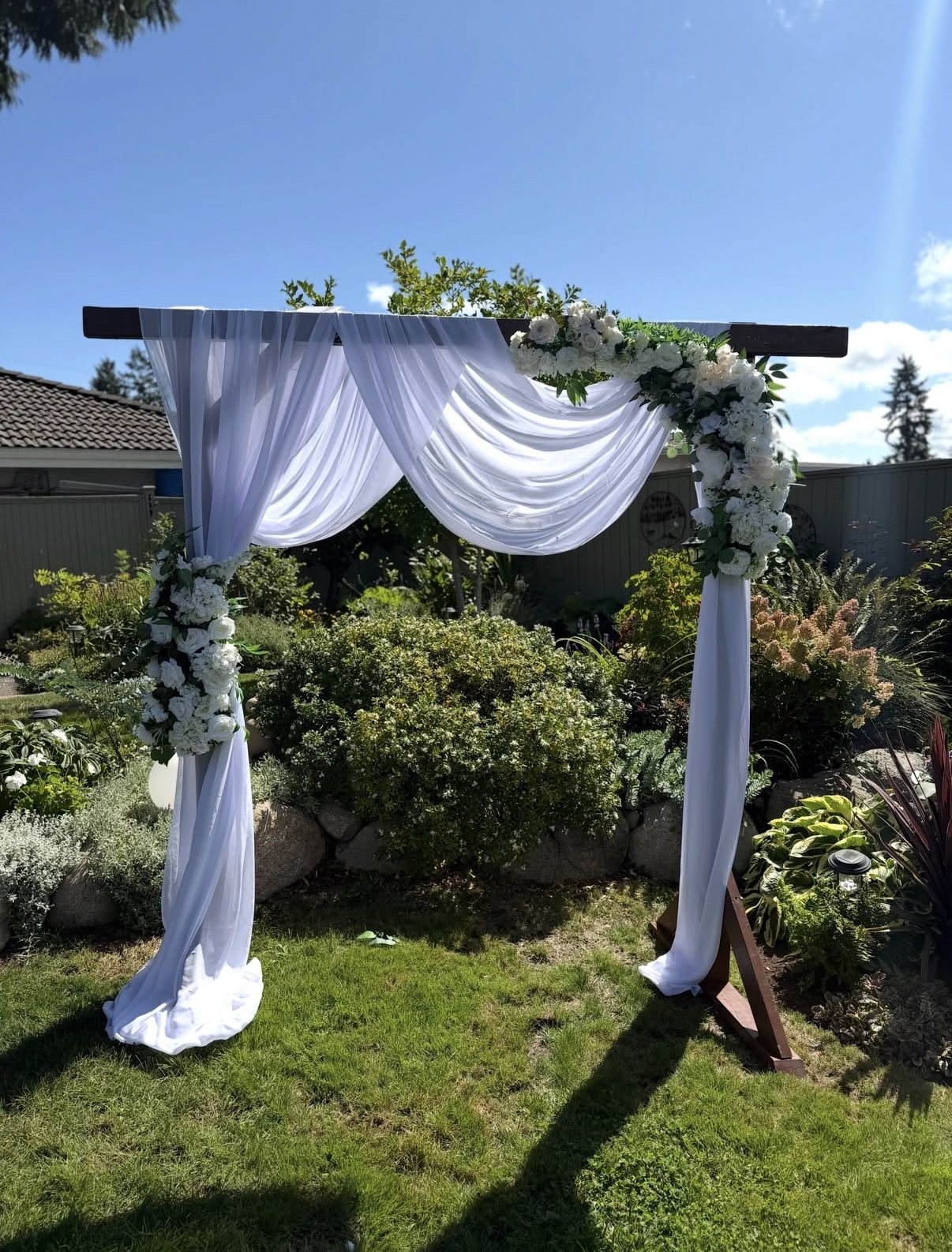 White draped wooden ceremony arch with white florals in a garden